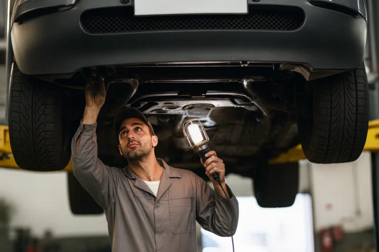 Mécanicien inspectant le dessous d’un véhicule sur un pont élévateur, illustrant les risques de rouler sans contrôle technique pour les chauffeurs VTC et taxis